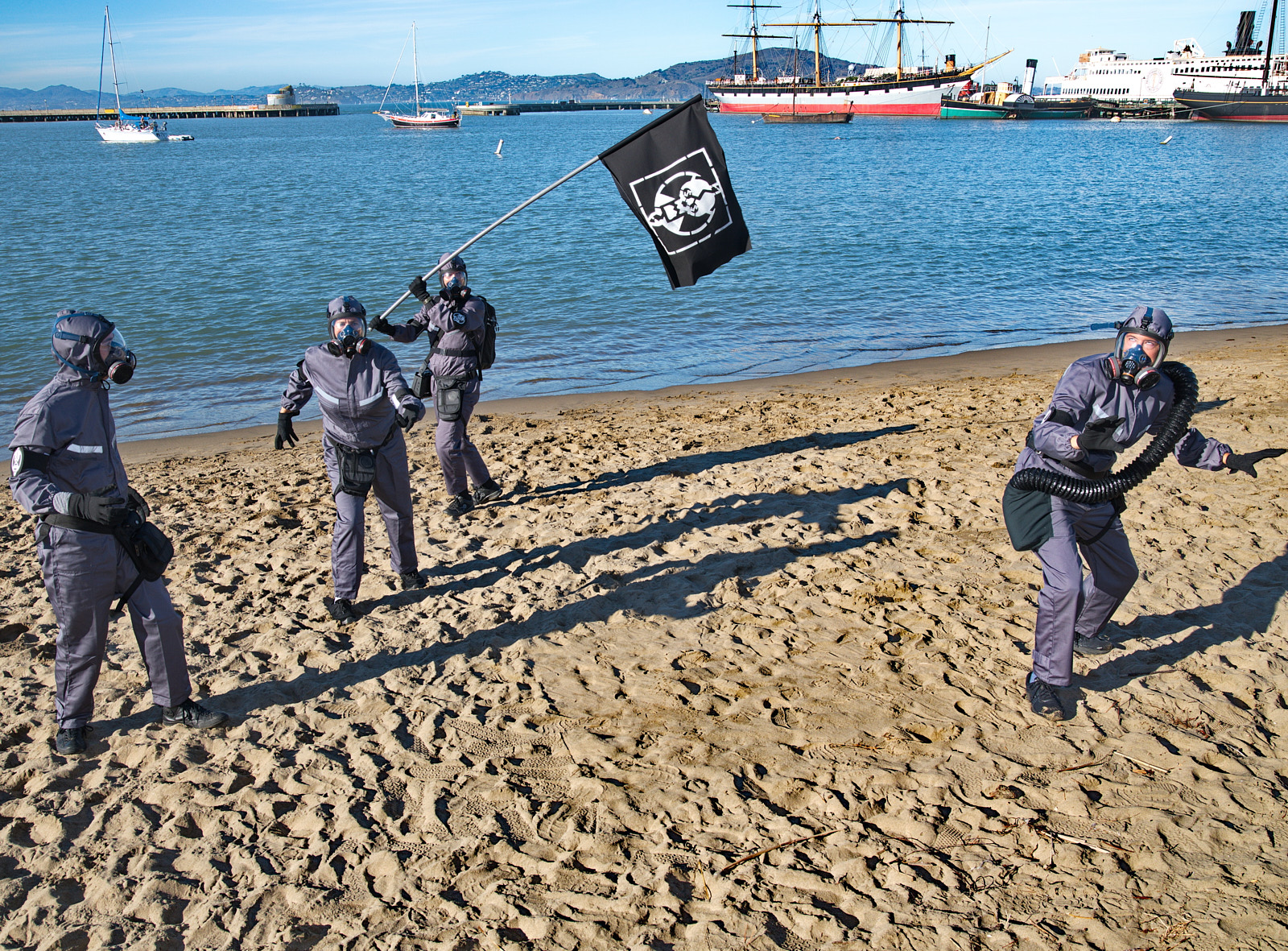 Xtractors dressed in grey hazmat suits stand on a beach with a black flag